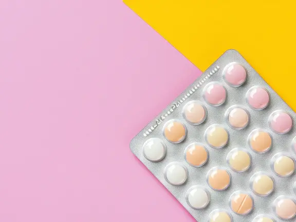 Eine Blisterpackung mit pastellfarbenen Pillen auf rosa und gelbem Hintergrund.
